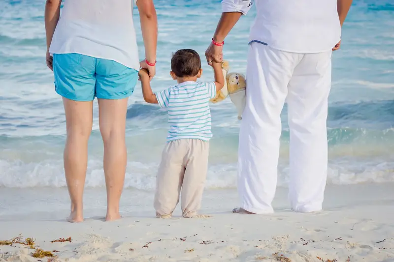 Family on beach with grandchild - Pros And Cons Of Living Near Family